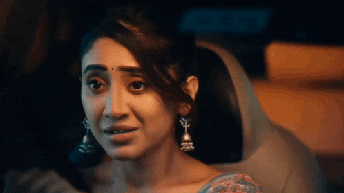 a woman wearing earrings is sitting in the back seat of a car looking at the camera .