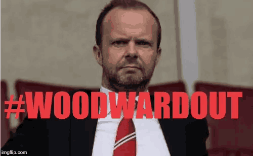 a man in a suit and tie is sitting in front of a sign that reads #woodwardout