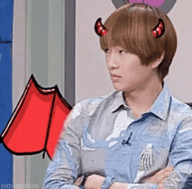 a young man with devil horns on his head is sitting with his arms crossed