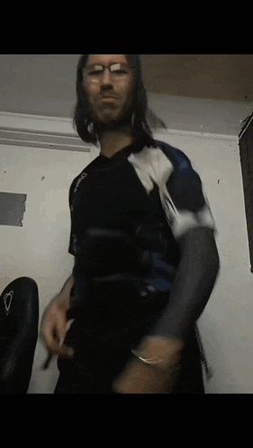 a man with long hair and glasses is wearing a black shirt with a white stripe on the sleeves