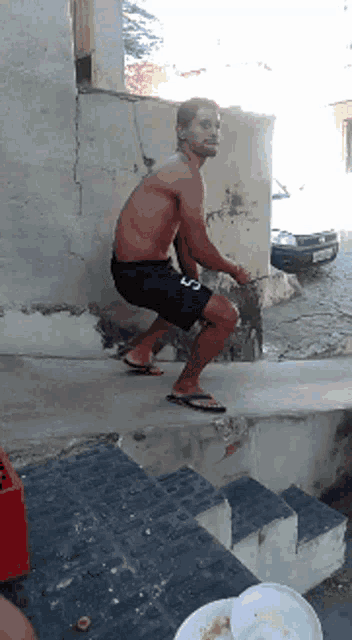 a shirtless man squatting on a set of stairs wearing flip flops