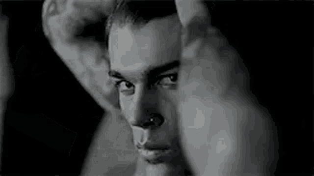 a black and white photo of a man with a nose ring and a tattoo on his face .