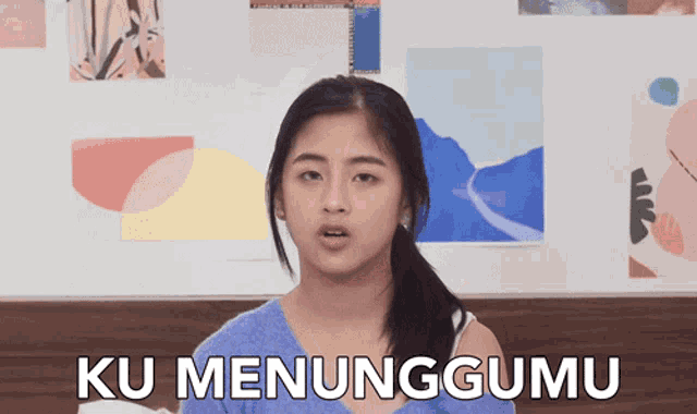 a woman says ku menunggumu in front of paintings