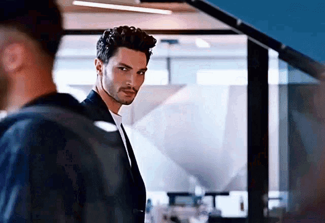 a man in a suit and tie is standing in front of a mirror .