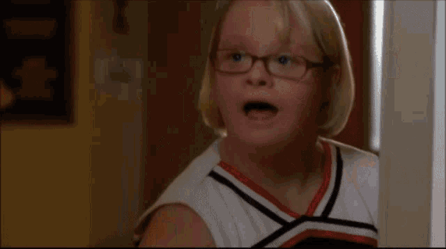 a girl wearing glasses and a cheerleading uniform is making a funny face