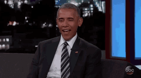barack obama is laughing while sitting on a couch in front of a television .