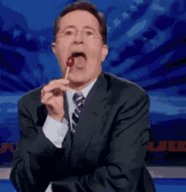 a man in a suit and tie is licking a lollipop in his mouth .