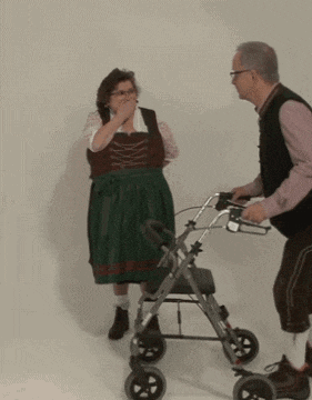 a man pushing a walker next to a woman in a green dress