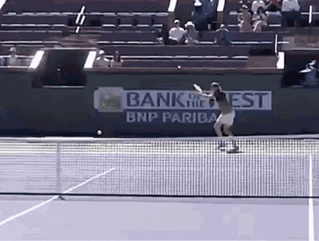 a tennis player swings his racket at a tennis ball in front of a bnp pariba banner