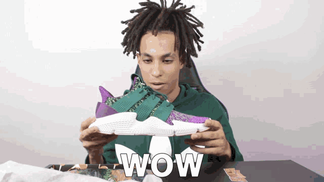 a man in a green hoodie is holding a pair of shoes and the word wow is on the bottom right