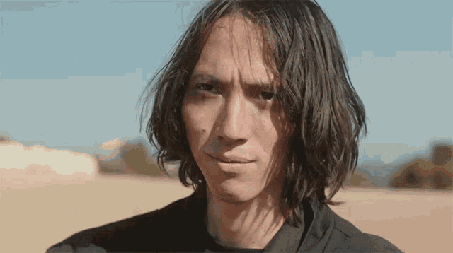 a young man with long hair is looking at the camera