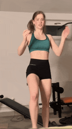 a young woman in a green sports bra and black shorts is jumping in the air