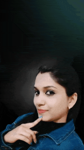 a woman in a blue jacket is smiling with her hand on her face