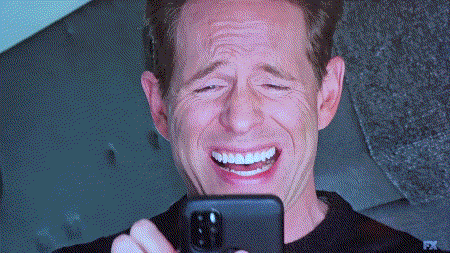 a man is laughing while holding a cell phone with fx written on the bottom