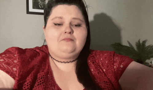 a woman wearing a choker and a red shirt looks at the camera