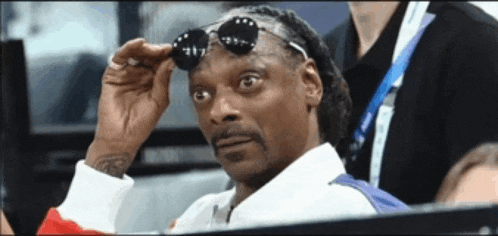 snoop dogg adjusts his sunglasses while sitting in the stands