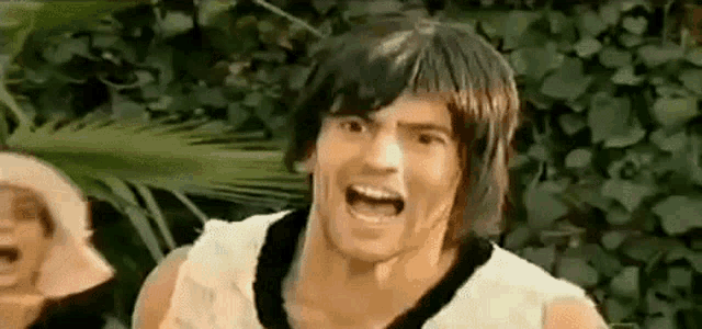 a man in a wig is making a funny face while standing in front of a bush .