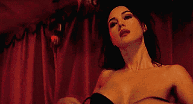 a woman is standing in front of a red curtain without a shirt on
