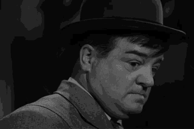a man wearing a hat and a suit looks down
