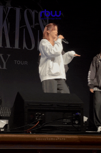 a woman singing into a microphone in front of a sign that says kiss