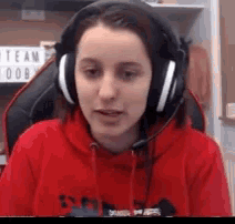 a woman wearing headphones and a red hoodie is looking at the camera .