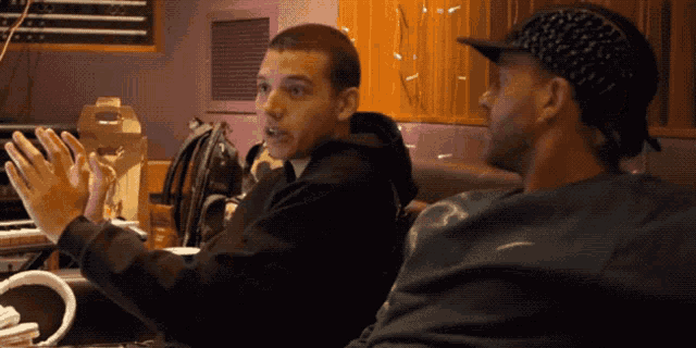 two men are sitting at a table with one wearing a black hat