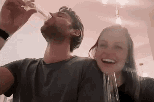 a man is drinking from a glass next to a woman who is laughing .