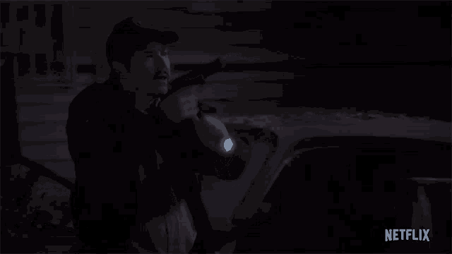 a police officer is holding a gun in front of a car at night .