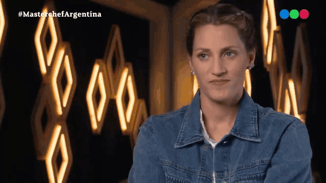 a woman in a denim jacket stands in front of a sign that says masterchefargentina