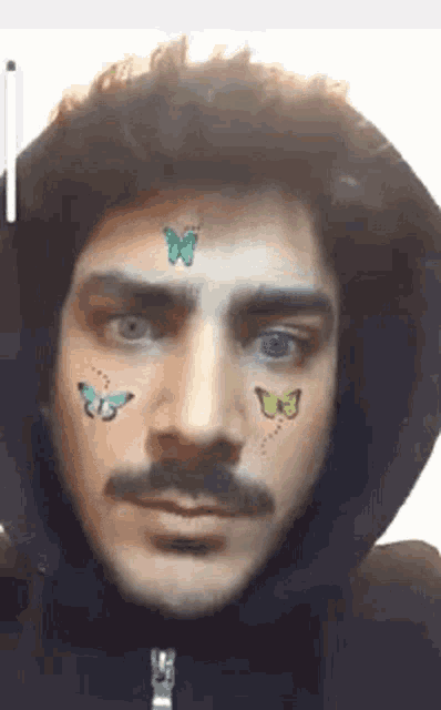a man with a mustache and butterflies on his face is wearing a black hoodie .