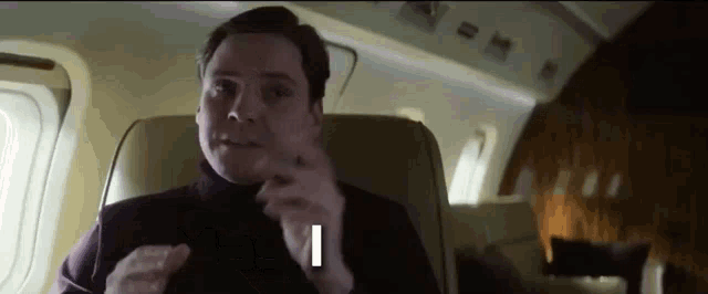 a man is sitting on a plane talking on a cell phone and making a funny face .