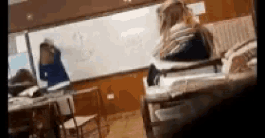 a group of people are sitting in a classroom with a whiteboard in the background .
