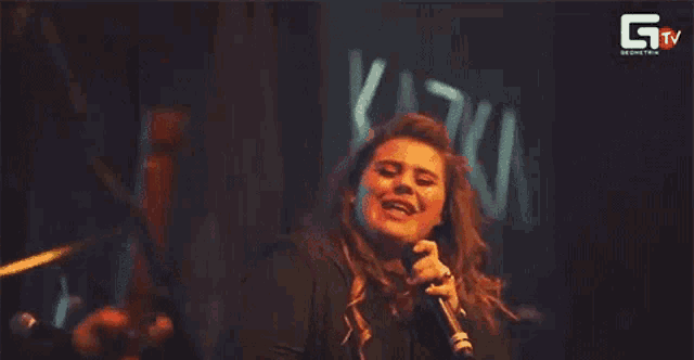 a woman is singing into a microphone in front of a crowd .