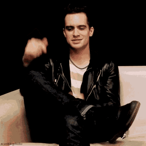 a man in a leather jacket is sitting on a couch with his legs crossed
