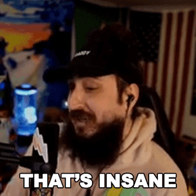 a man with a beard is sitting in front of a microphone and saying `` that 's insane ''