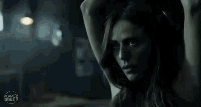 a woman is standing in a dark room with her arms behind her head .