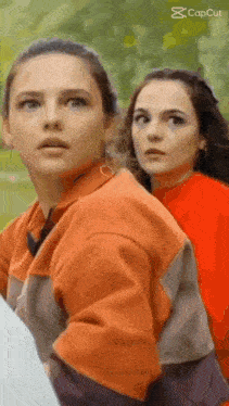 two women are standing next to each other in a park .