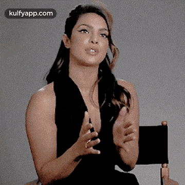 a woman in a black dress is sitting in a director 's chair with her hands out .