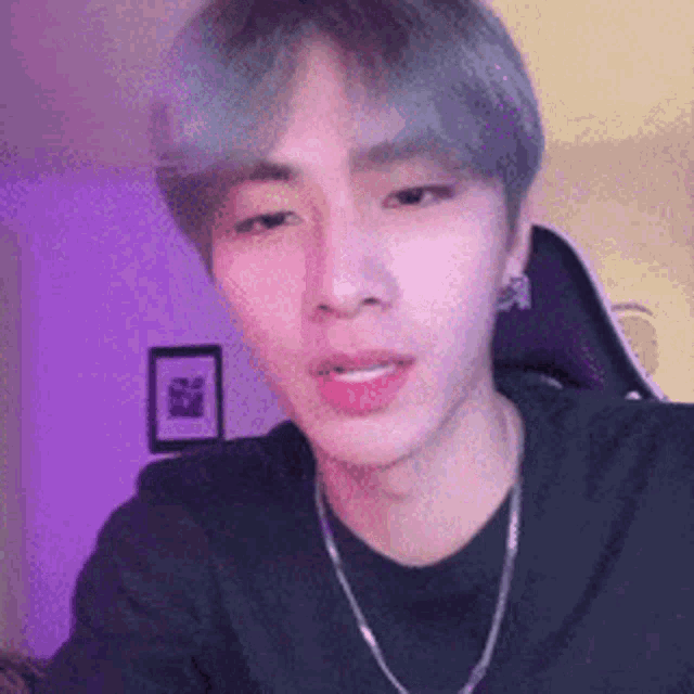 a young man wearing a black shirt and a silver chain around his neck is looking at the camera .