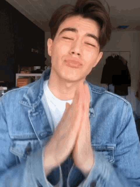 a young man in a denim jacket is making a face with his hands folded