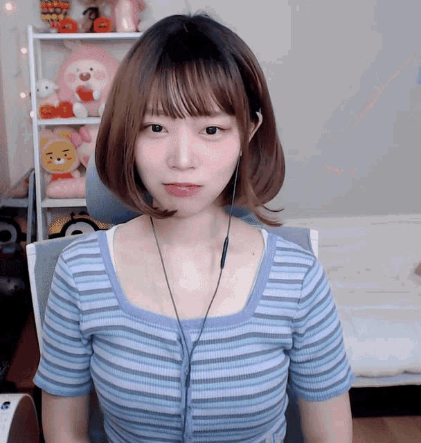 a girl wearing a blue striped shirt is sitting in front of a stuffed animal shelf