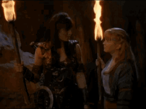 two women are standing next to each other with a torch in the background