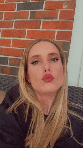 a woman with long blonde hair is making a funny face in front of a red brick wall