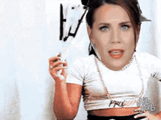 a woman in a white crop top is holding a stick with her face on it .