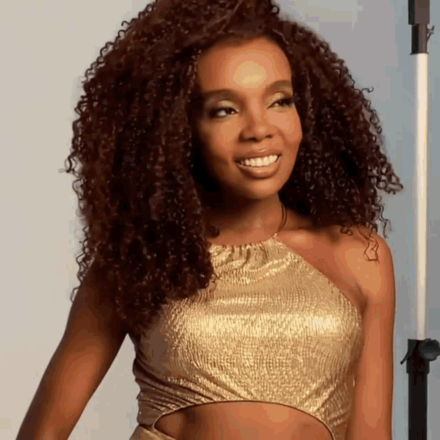 a woman with curly hair wears a gold top