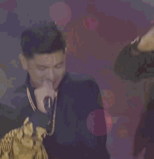 a man singing into a microphone with a necklace that says n on it