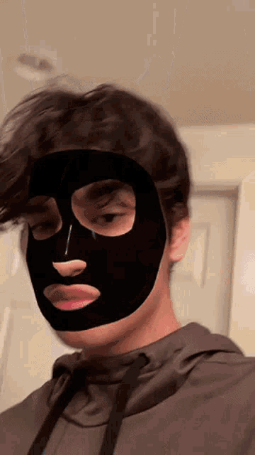 a man with a black mask on his face looks at the camera