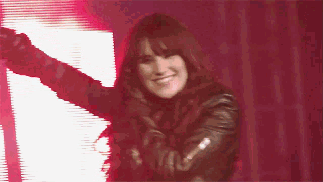 a woman in a black leather jacket is smiling in front of a red background