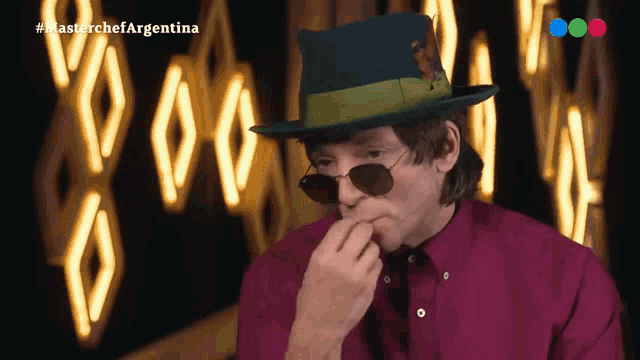 a man wearing a hat and sunglasses is eating something in front of a sign that says master chef argentina