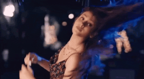 a woman is dancing in a dark room with her hair flying in the wind .